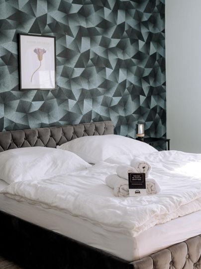 A stylish bedroom with an upholstered bed and elegant bedding. The geometric wallpaper and artwork give the room a modern touch.