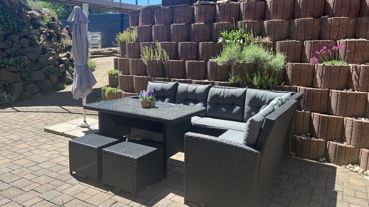 Een gezellige zitruimte in de buitenlucht met een modern rattanbank en planten. Op de achtergrond is een licht betegelde muur te zien.