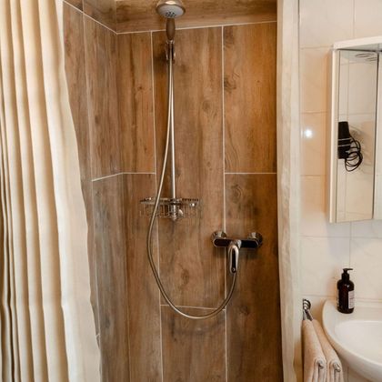 A modern shower with wood-look walls and a glass wall. On the side, a mirror and a towel rack are visible.