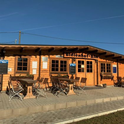 Wooden building of the Bielenhof-Alm with tables and chairs outside.