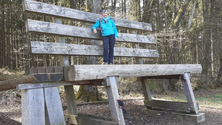 Une personne se tient sur un banc de bois surdimensionné dans la forêt.