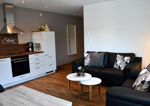 Un appartement moderne avec une cuisine ouverte et un coin salon confortable. Les meubles sont dans des couleurs neutres, avec deux petites tables au centre.
