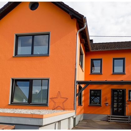 Ein leuchtend orangefarbenes Haus mit unterschiedlichen Fenstern und Eingangstür. Die Fassade hat eine moderne und einladende Ausstrahlung.