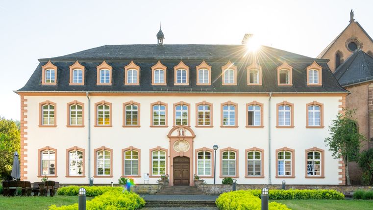 Historisches Gebäude mit symmetrischer Fassade und Sonnenschein im Hintergrund.