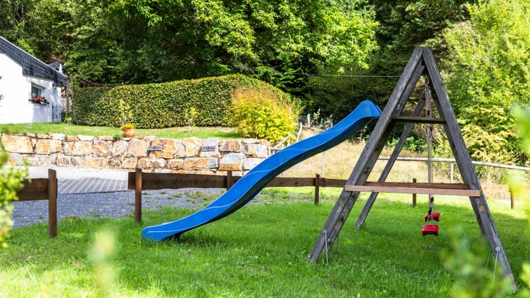 A slide in a green garden with trees in the background. The playground is quiet and inviting.