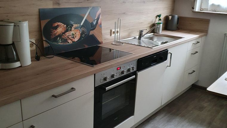 A modern kitchen with bright cabinets and wooden details. It is well equipped with a stove, a sink, and a coffee maker.