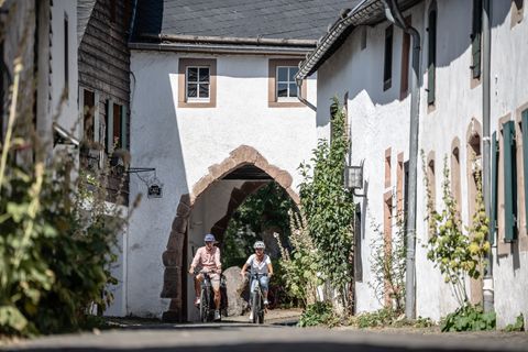 Deux cyclistes casqués traversent le village historique de Kronenburg en passant par un groupe de maisons.