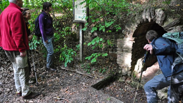 Des randonneurs observent un panneau d'information et un ancien tunnel sur le sentier de randonnée du canal romain.