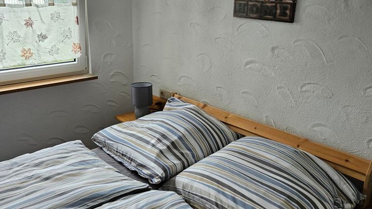 A cozy bedroom with a double bed and striped bedcovers. A picture hangs on the wall, and the window lets daylight in.