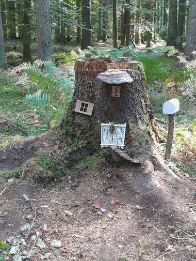 Une souche d'arbre avec de petites maisons en bois et un panneau se trouve dans la forêt. L'endroit semble pittoresque et accueillant.