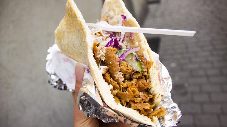 A döner held in one hand, filled with meat, salad, and sauce, wrapped in aluminum foil.