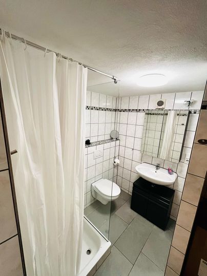 Een moderne badkamer met een douche, een toilet en een wastafel. De muren zijn versierd met witte tegels en een grote spiegel.
