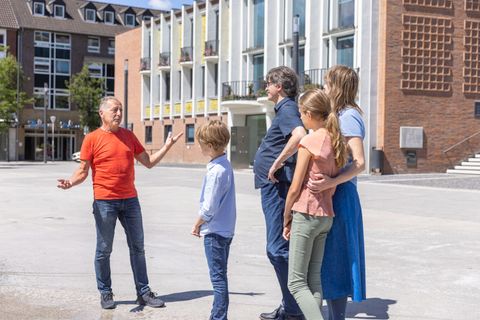 Eine Gruppe von Menschen steht im Freien und spricht miteinander. Im Hintergrund sind moderne Gebäude zu sehen.