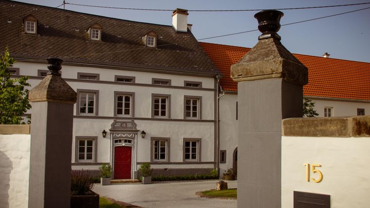 A stylish building with a red door and large windows. It is surrounded by a wall with columns and features an inviting entrance.