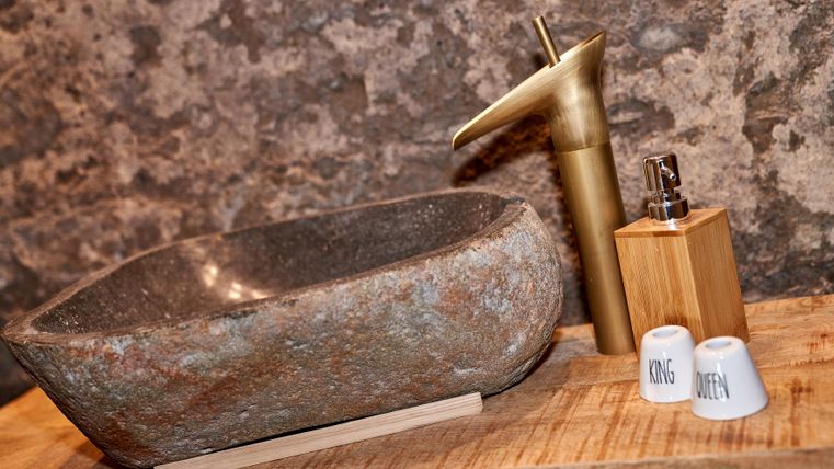 Ein elegantes Waschbecken aus Stein mit einem goldenen Wasserhahn. Daneben steht eine Holzflasche und zwei kleine Behälter.