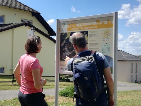 Two people are looking at a hiking board outdoors.