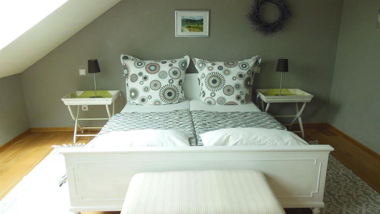 Ein gemütliches Schlafzimmer mit einem weißen Bett und stilvollen Kissen. Neben dem Bett stehen zwei Nachttische mit modernen Lampen.
