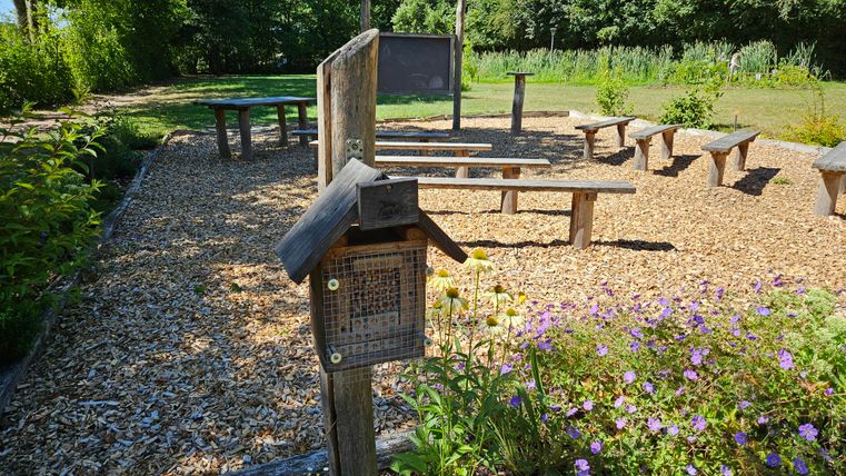 Un espace extérieur confortable avec des sièges et des tables en bois. Au premier plan se trouve une petite boîte et des fleurs colorées.