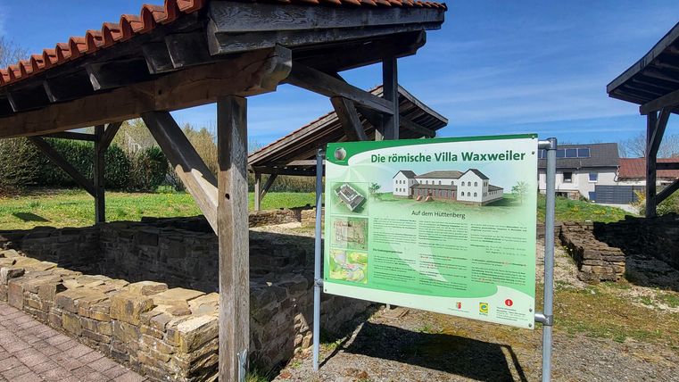 Ein übersichtlicher Informationsbereich über die alte Villa Waxweiler mit Erklärungen zur Geschichte. Im Hintergrund sind die restaurierten Grundmauern der Villa sichtbar.