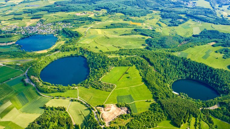 Een indrukwekkend landschap met twee ronde meren omringd door groene velden en bossen. Het uitzicht toont een natuurlijke schoonheid en uitgestrekte heuvelachtige gebieden.