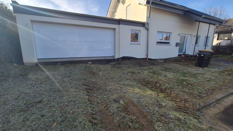 Une maison individuelle moderne avec un grand garage. Le jardin est bien entretenu et le ciel est dégagé.