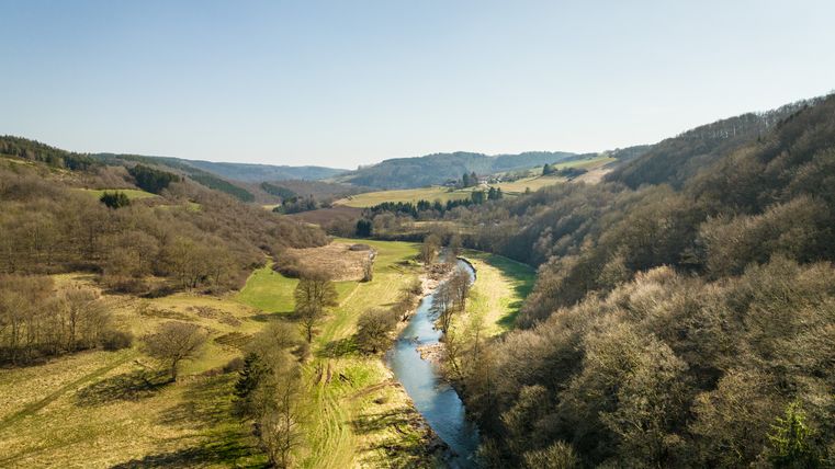 Paysage avec rivière, prairies et collines sous un ciel bleu.