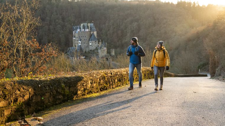 Twee wandelaars op een pad met kasteel Eltz op de achtergrond.