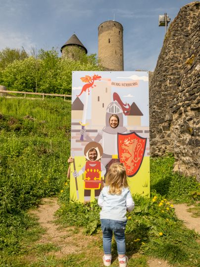 Un enfant se tient devant un stand de photos avec des chevaliers et un dragon sur les ruines du château de Nürburg.