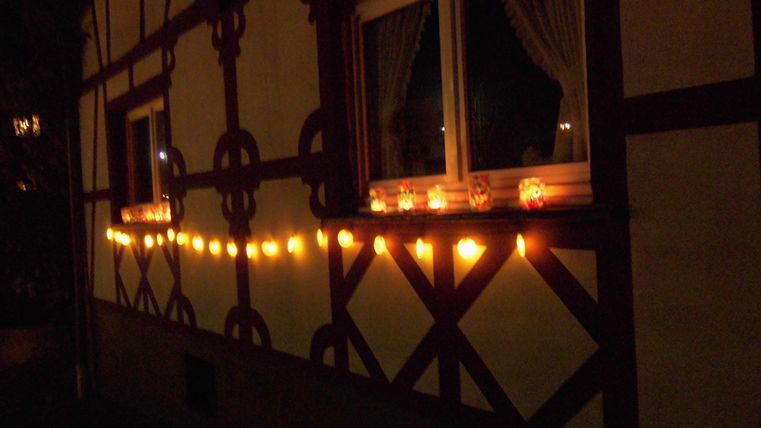 A cozy house with illuminated windows and a string of lights. The warm lights create an inviting atmosphere at night.