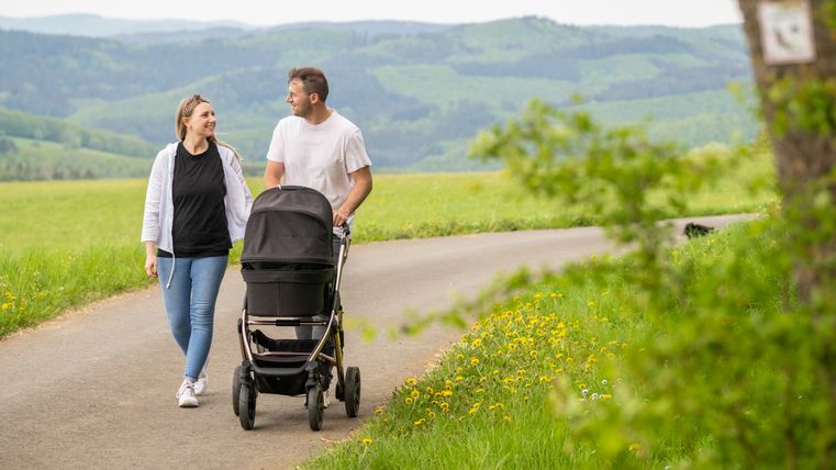 Een stel wandelt met een kinderwagen over een pad in een groen landschap.
