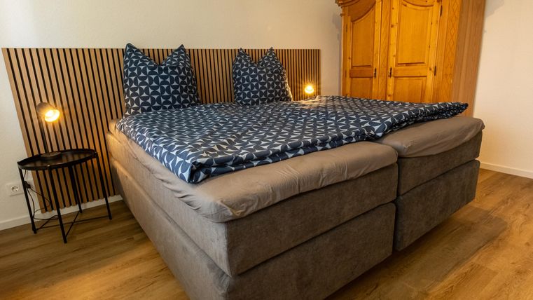 Een gezellige slaapkamer met een groot, comfortabel bed en blauwe kussens. Een houten commode en zachte verlichting aanvullen de sfeer.
