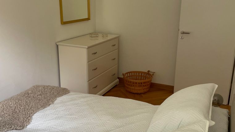 Une chambre simple avec un lit, une commode et un panier rond. Un miroir est accroché au mur dans un cadre doré.