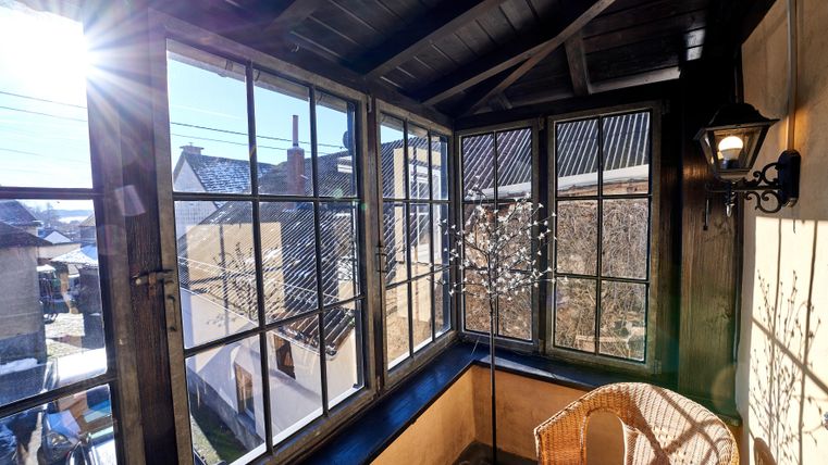 Ein gemütlicher Balkon mit großen Fenstern und einem Sitzbereich aus Rattan. Die Sonne strahlt durch die Fenster und schafft eine einladende Atmosphäre.