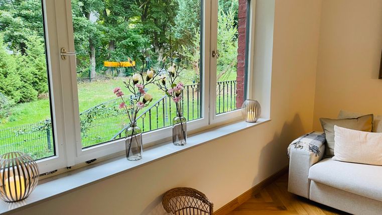 Une pièce confortable avec une fenêtre donnant sur un jardin verdoyant. Sur le rebord de la fenêtre, il y a des vases avec des fleurs et des lampes décoratives.