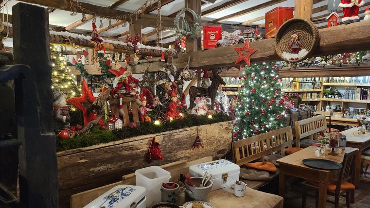 Une pièce confortablement décorée pour la période de Noël avec un sapin de Noël et des décorations festives. Sur les tables se trouvent diverses gourmandises et l'ambiance est accueillante.
