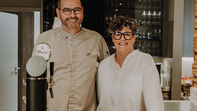 Jörg en Jessica Frankenbach staan achter de bar. Ze glimlachen en zijn de gastheer en gastvrouw van Hotel Panorama.