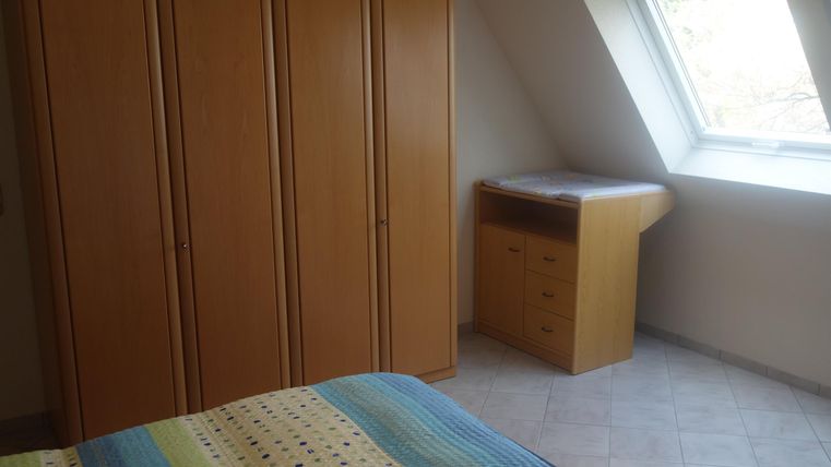 A simple bedroom with a large wardrobe and a desk. The room has a skylight that lets in daylight.