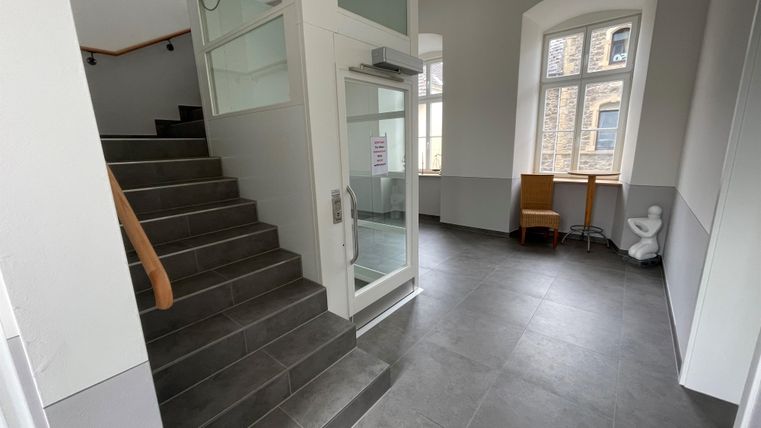 Un hall d'entrée moderne avec un escalier et de grandes fenêtres. Il y a une petite table et une chaise dans le coin.