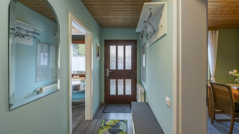 Een uitnodigende entree met een groene muur en een houten plafond. De ruimte beschikt over een garderobe en een gezellige zithoek.
