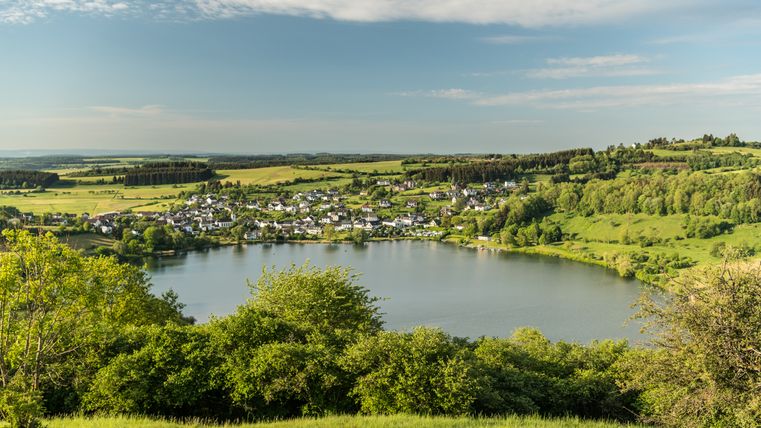 View of the Schalkenmehren maar in the Eifel with surrounding village and green landscape.