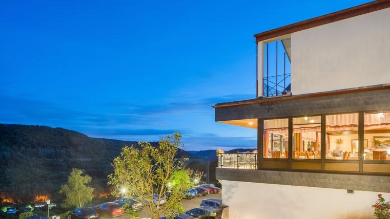 Het Waldhotel Sonnenberg 's Avonds met grote ramen. Op de achtergrond is een rustige landschap en geparkeerde auto's te zien.