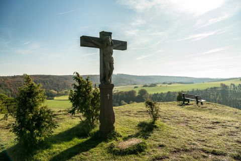 Kreuz auf einem Hügel mit Bank und weiter Landschaft im Hintergrund.