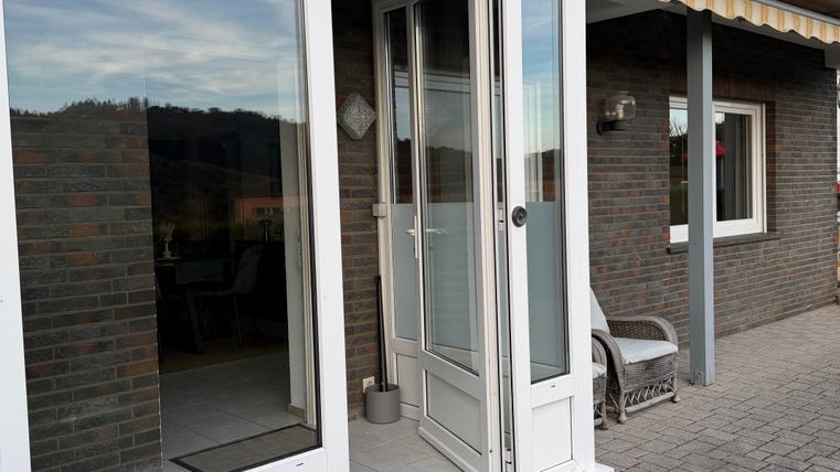 An entrance area with a bright door and large windows. Next to the door is a cozy chair and in the background several windows are visible.