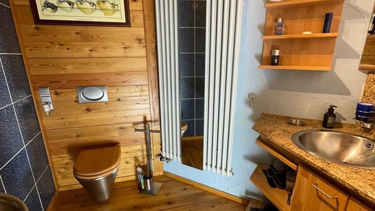 A modern bathroom with wood paneling and a sink. There is a shower and a shelf with care products.