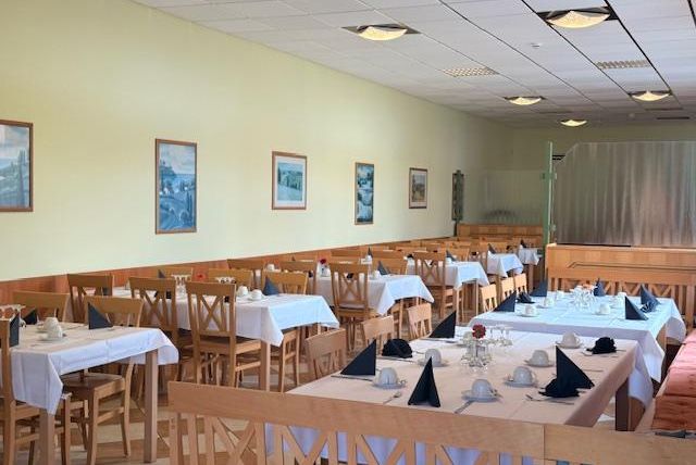 A bright restaurant with several tables covered with white tablecloths. Pictures hang on the wall and the atmosphere feels friendly and inviting.