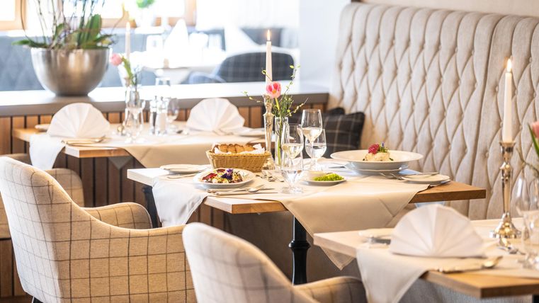 An elegant restaurant with stylish tables and comfortable chairs. The table decoration includes flowers and set dishes, creating a pleasant atmosphere.
