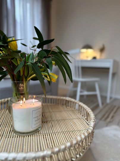 Een gezellige woonkamer met een gevlochten tafel. Op de tafel staat een brandende kaars en een bloemstuk.