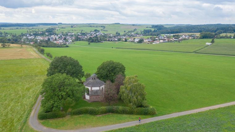 Landschaft mit Kapelle und Dorf im Hintergrund.