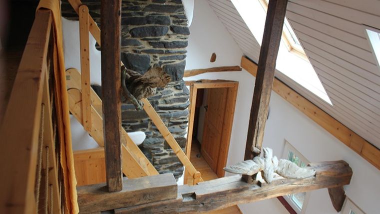 Een helder, modern chalet met houten balken en een stenen open haard. De ruimte heeft grote ramen en een uitnodigende sfeer.