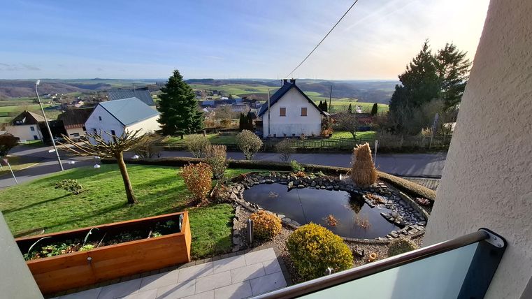 Une belle vue sur un environnement rural avec un étang et plusieurs maisons. Le paysage est vert et entouré d'arbres.